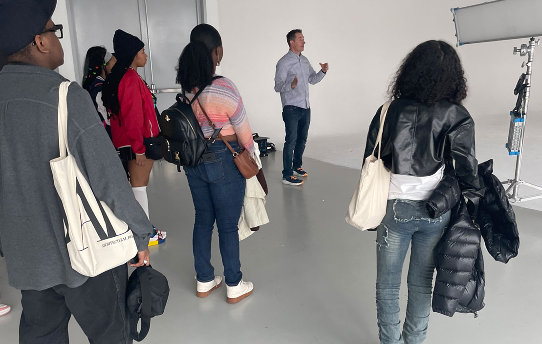 A media arts project class top to a video sound stage - a group of students faces a teacher